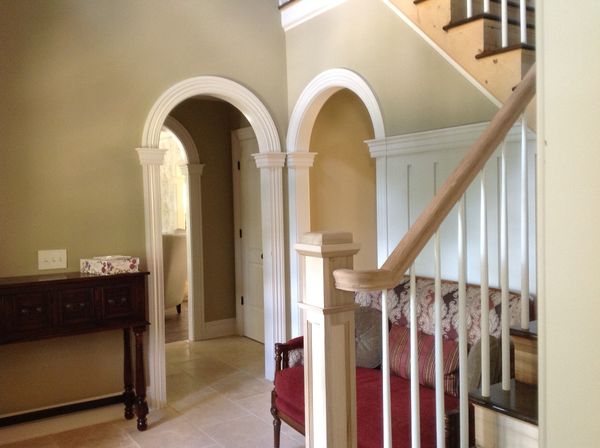 Entry hall with two arched doorways trimmed with fluted pilasters, beside a staircase with a square newel post and paneled wall