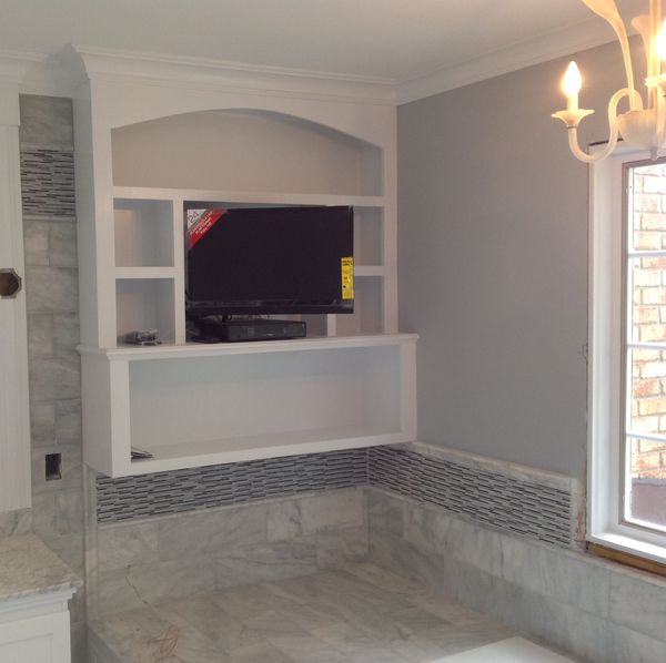 White built-in bathroom unit with an arched top niche, shelves around a TV and a floating open shelf, finished with crown moulding