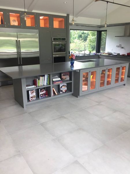 Custom kitchen built and installed by DMM Carpentry: side of the gray island with open bookshelves and orange-lit glass-front cabinets, with a corner window behind