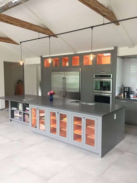Custom kitchen built and installed by DMM Carpentry: gray cabinetry with orange-lit glass-front cabinets, a large island, and a wall of cabinets around a stainless fridge and wall ovens