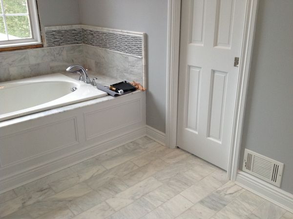 Paneled bathtub front with baseboard, next to a six-panel interior door with casing