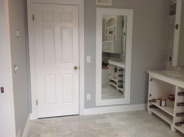 Six-panel interior door with wide casing beside a trimmed wall mirror and baseboard in a bathroom